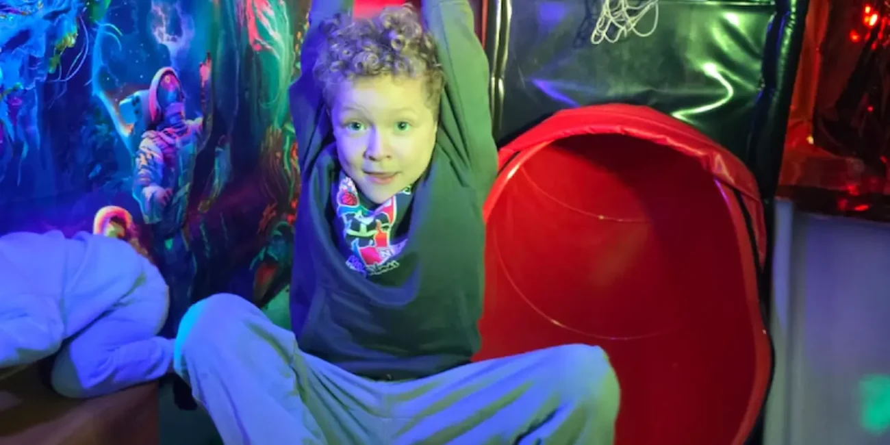 Child playing on climbing rings inside the Essex Soft Play Bus soft play area with colourful tunnel slide and indoor play equipment.