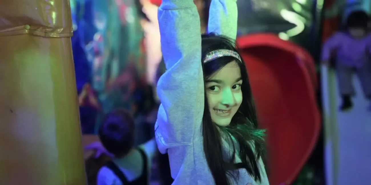 Child playing on climbing rings inside the Essex Soft Play Bus soft play area with colourful slide and indoor play equipment.