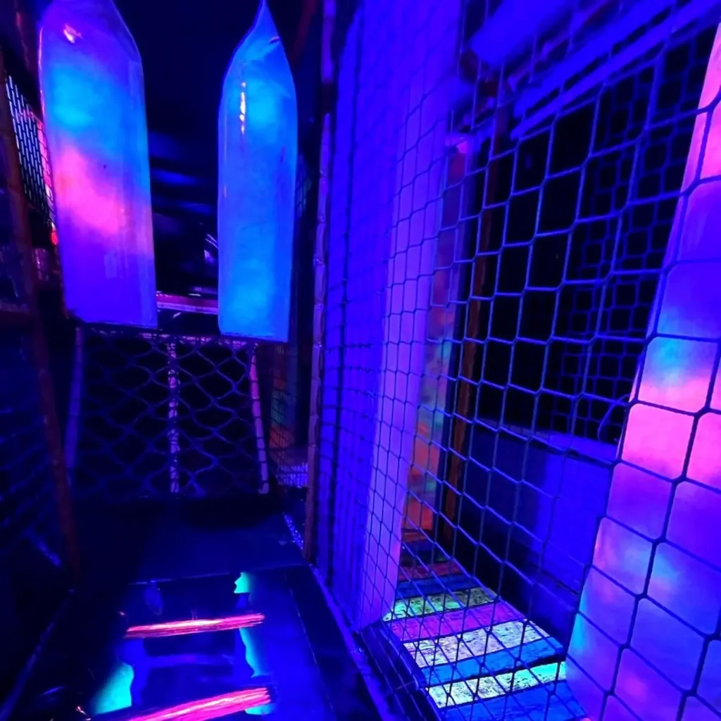 Neon soft play climbing frame and tunnel area inside the Essex Soft Play Bus with colourful UV lighting and indoor play equipment.