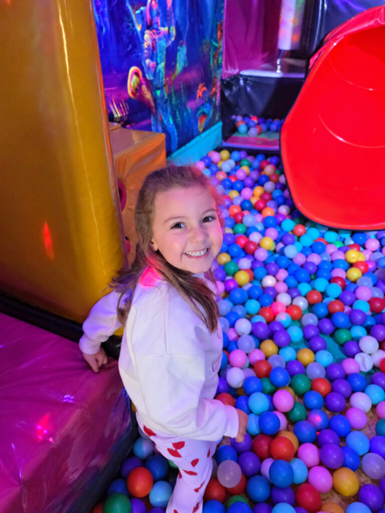 Smiling child beside the colourful ball pit and red slide inside Essex Soft Play Bus