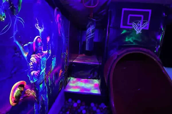 Neon Soft Play Interior Inside the Essex Soft Play Bus Neon soft play interior inside the Essex Soft Play Bus featuring colourful UV lighting, play tunnel and basketball hoop for children’s parties in Essex.