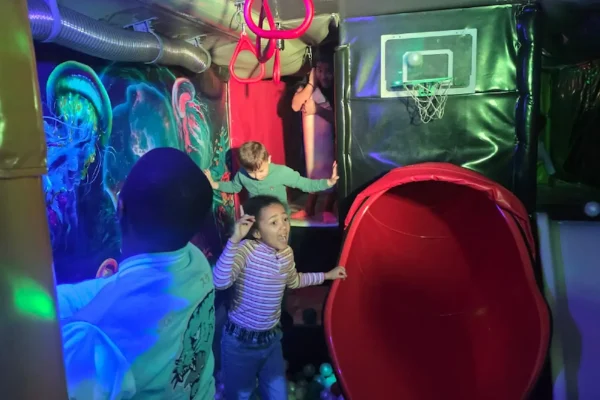 Children Playing in the Slide Area Inside the Essex Soft Play Bus Children playing in the slide play area inside the Essex Soft Play Bus with climbing steps and mini basketball hoop.